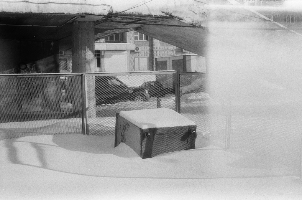 Black and white photo of a snowy yard surrounded by a fence.