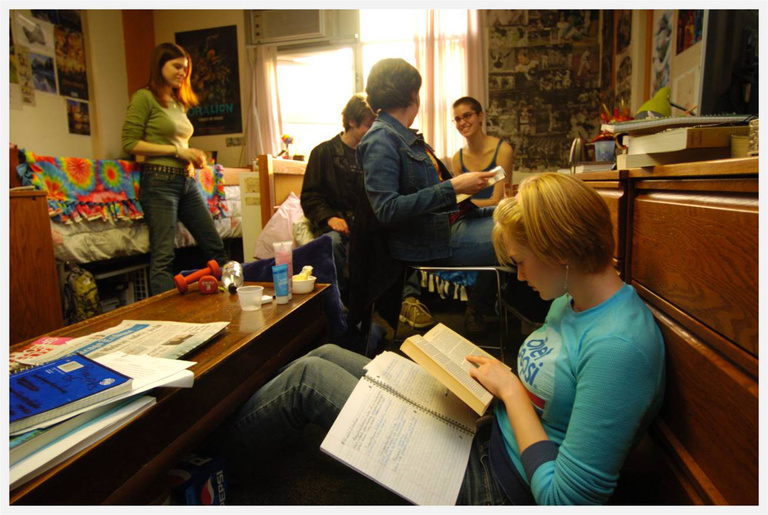 three students in a dorm room laughing with books