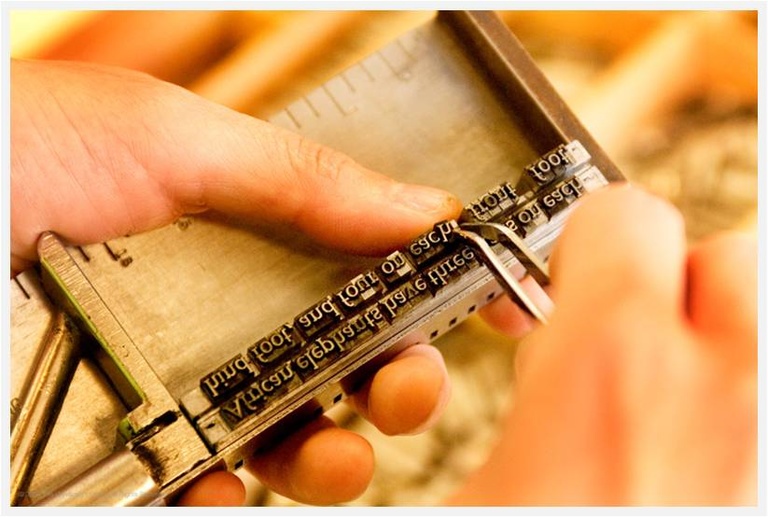 close up of hands setting type in a wooden box